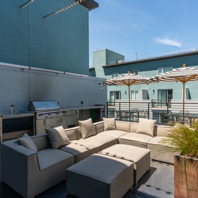 Domain Oakland Apartments - rooftop sky deck with outdoor couches, tables, and a grilling station