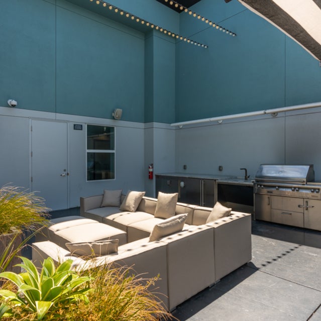 Domain Oakland Apartments - rooftop sky deck with outdoor couches, tables, and a grilling station